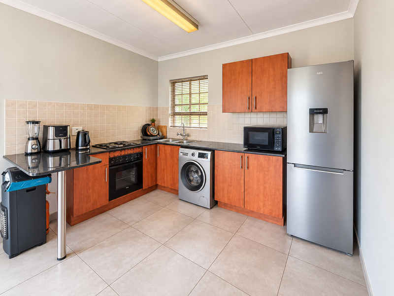 A functional kitchen featuring wood-finish cabinetry, granite countertops, tiled backsplash, and integrated appliances including an oven, hob, and washing machine.
