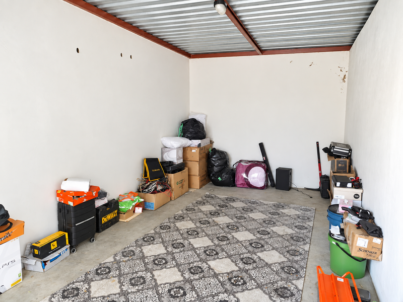 A functional garage space featuring a corrugated metal ceiling, concrete flooring, and exposed steel beams, currently utilized for storage.