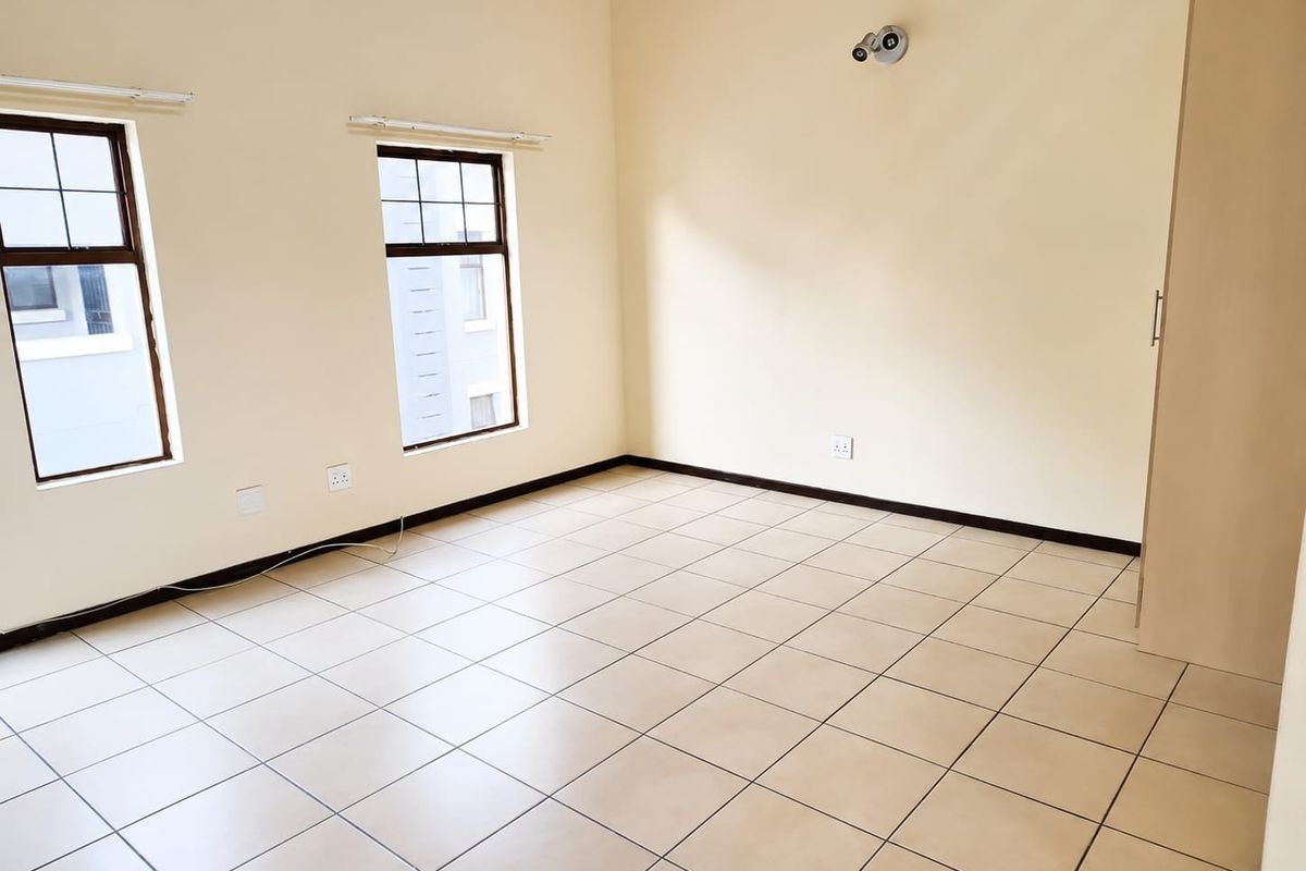 A bright, empty bedroom featuring neutral tiled flooring, built-in cupboards, and large windows that provide ample natural light.
