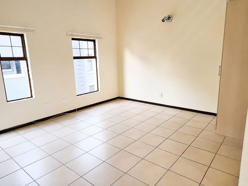 A bright, empty bedroom featuring neutral tiled flooring, built-in cupboards, and large windows that provide ample natural light.