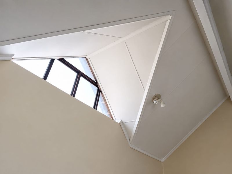 A view of a vaulted ceiling featuring a triangular window and a fixed spotlight fixture.