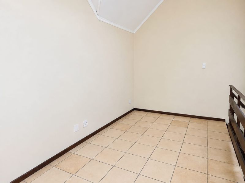 An empty bedroom featuring tiled flooring, a vaulted ceiling, and a timber balustrade overlooking the lower level.