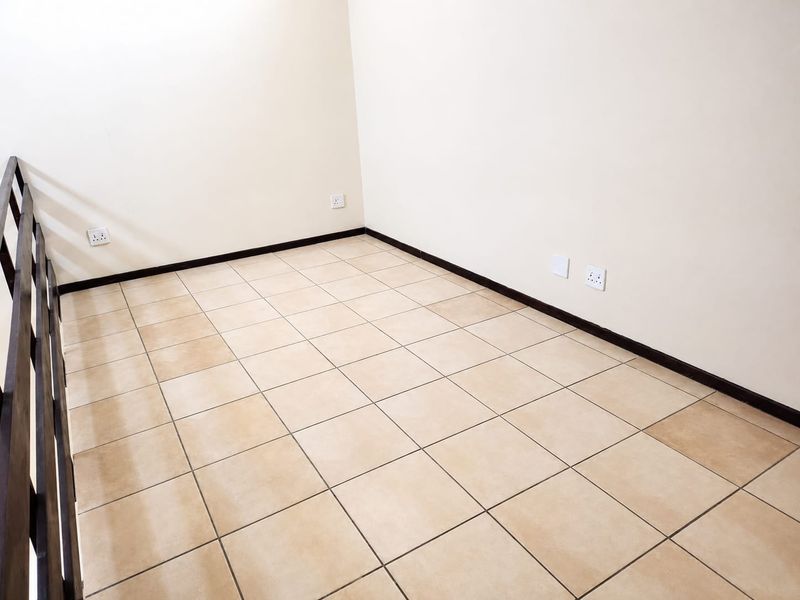 An empty bedroom space featuring neutral tiled flooring, clean walls, and a dark wooden staircase railing.