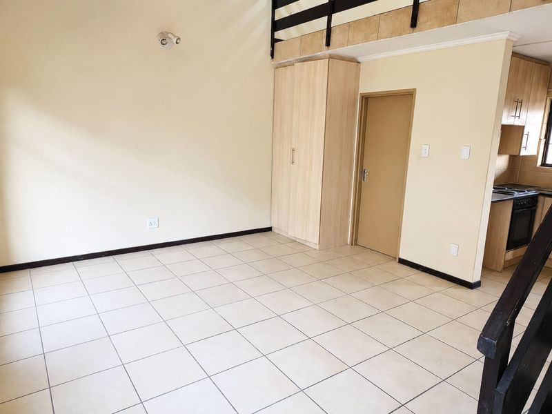 An open-plan living area featuring tiled floors, a built-in cupboard, and a mezzanine level, with an adjacent kitchen area.