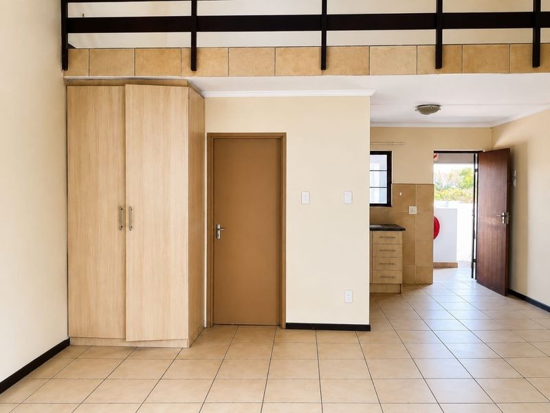 Open plan living area featuring tiled flooring, a built-in wardrobe, and a mezzanine level, with direct access to an adjoining kitchen and outdoor space.