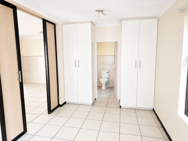 A bright, empty bedroom featuring neutral tiled flooring, ample built-in cupboard storage, and direct access to an en-suite bathroom.