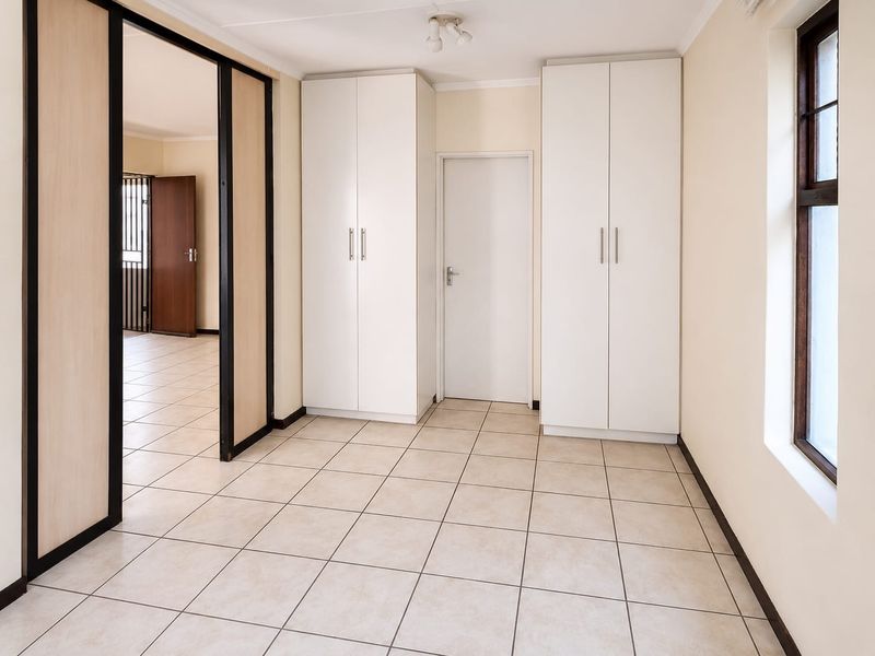 A bright, empty bedroom featuring neutral tiled flooring, built-in white cupboards, and a sliding door leading to an adjacent room.