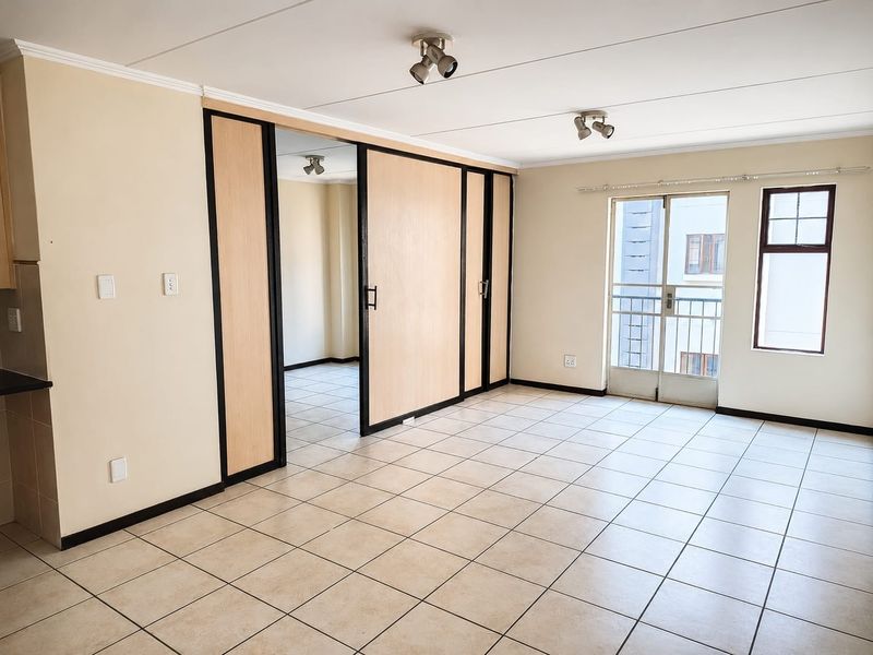 Spacious living area featuring neutral tiled flooring, ceiling spotlights, and a sliding room divider, with direct access to a balcony through a glass door.