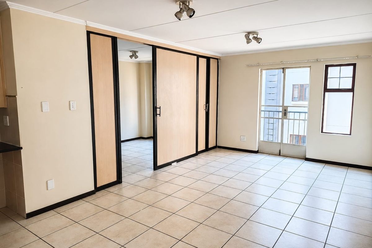 Spacious living area featuring neutral tiled flooring, ceiling spotlights, and a sliding room divider, with direct access to a balcony through a glass door.