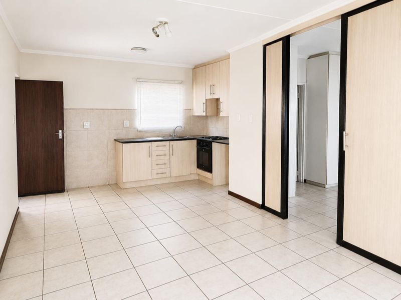 An open-plan kitchen and living area featuring light wood cabinetry, tiled flooring, and neutral walls, offering a clean and functional space.