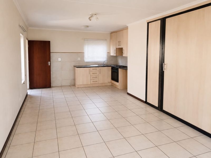 An open-plan living and kitchen area featuring tiled flooring, built-in cabinetry, and integrated kitchen appliances in a clean, vacant space.