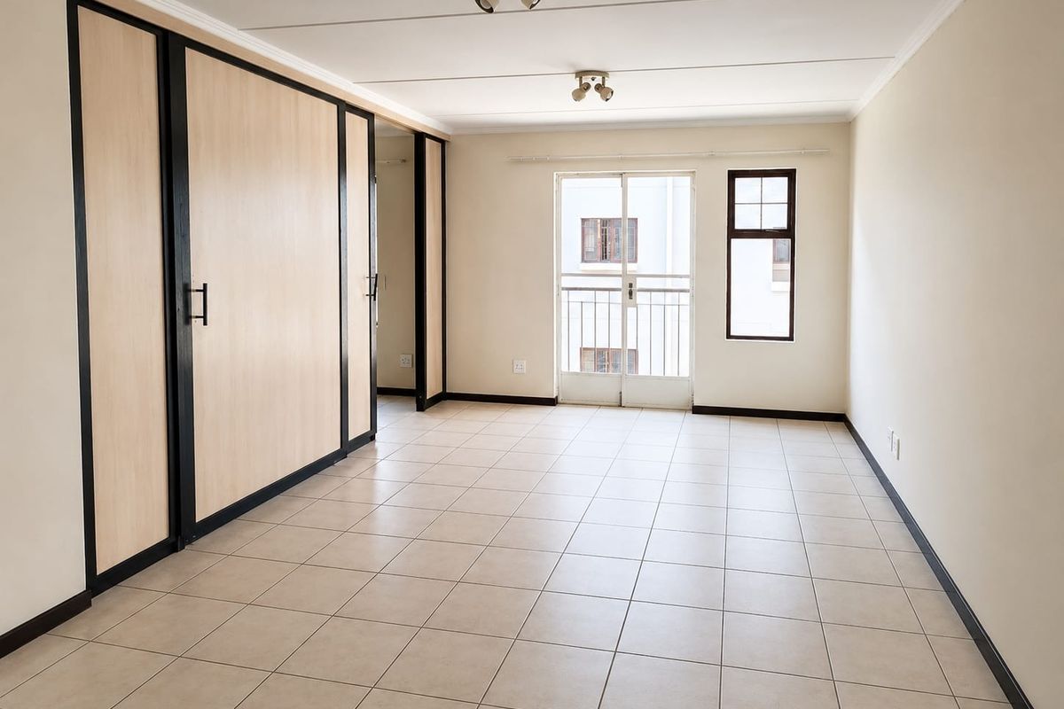 A bright, empty bedroom featuring neutral tiled flooring, built-in cupboards with modern trim, and a sliding door leading to a small balcony.