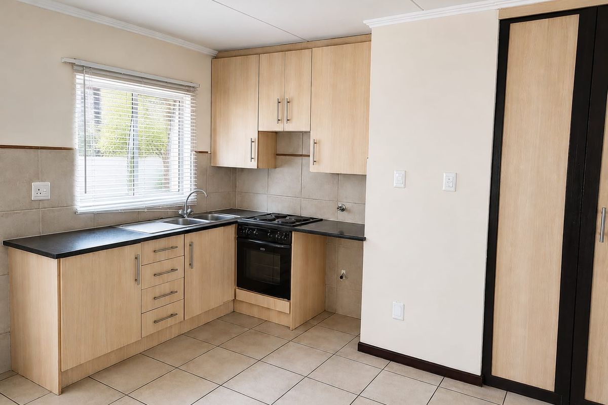 A clean, functional kitchen featuring light wood-finish cabinetry, black countertops, built-in oven and hob, tiled backsplash, and neutral floor tiles.