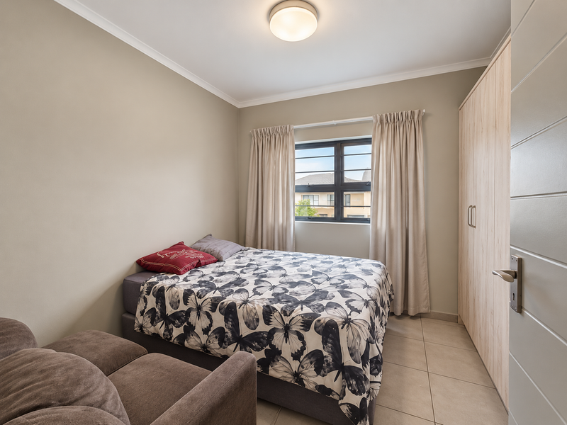 A well-maintained bedroom featuring neutral wall tones, tiled flooring, and a built-in wardrobe, offering a clean and functional living space.