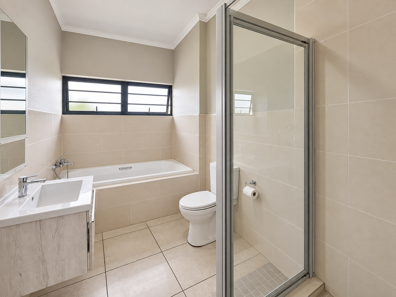A clean, modern bathroom featuring a built-in vanity, bathtub, separate shower enclosure, and neutral floor-to-ceiling tiling.
