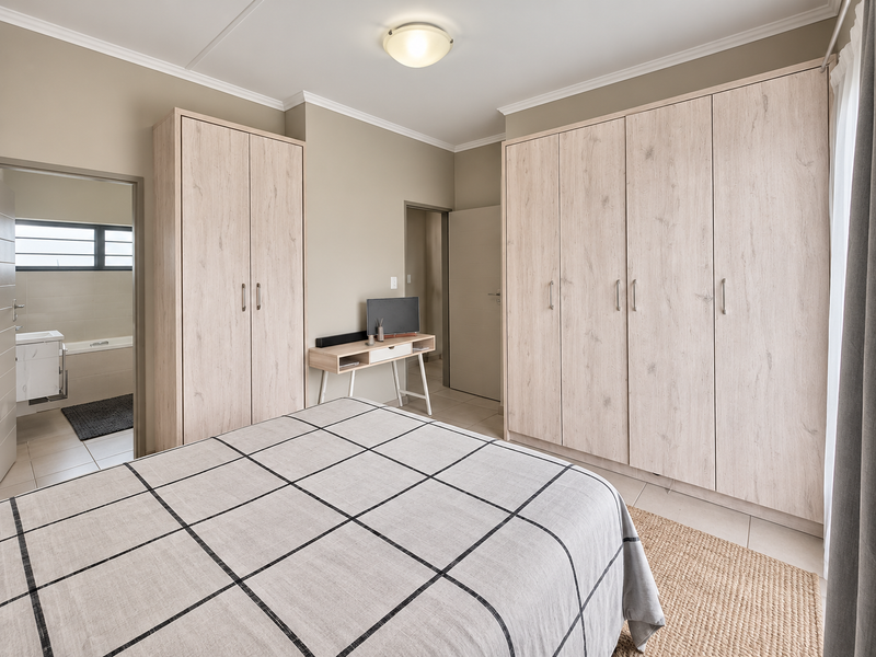 A well-maintained bedroom featuring light wood-grain built-in wardrobes, neutral wall tones, and direct access to an adjoining en-suite bathroom.