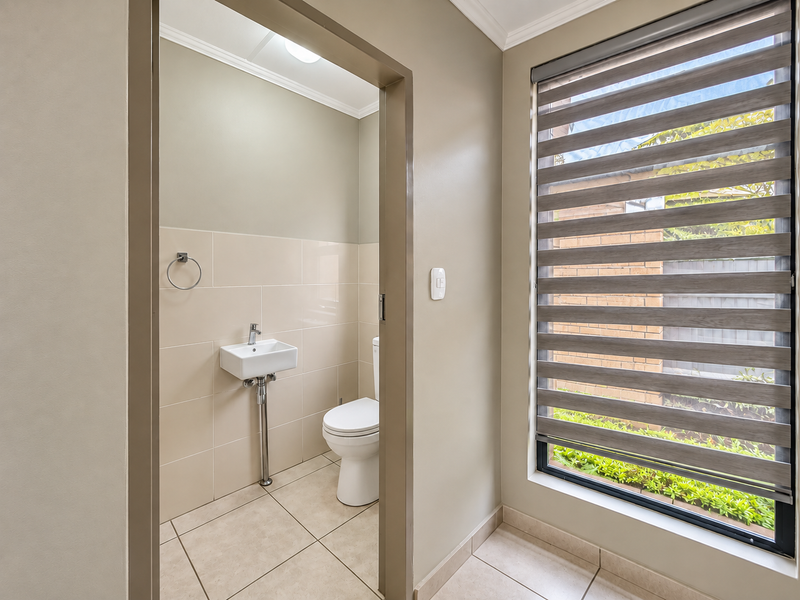 A clean and modern guest powder room featuring a wall-mounted basin, toilet, and neutral tiled finishes with a large window providing natural light.