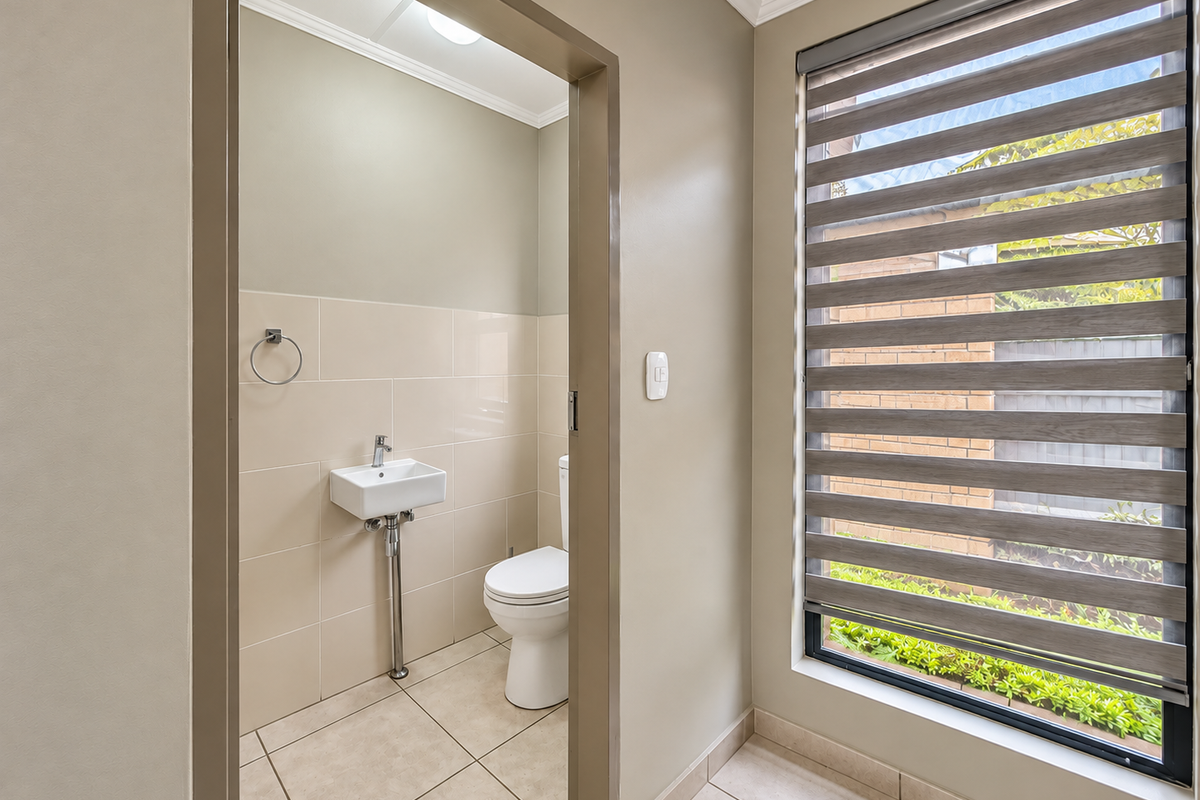 A clean and modern guest powder room featuring a wall-mounted basin, toilet, and neutral tiled finishes with a large window providing natural light.