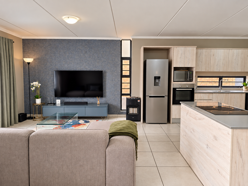 Modern open-plan living area featuring a contemporary kitchen with light wood cabinetry, integrated appliances, and a spacious island, seamlessly flowing into the lounge.
