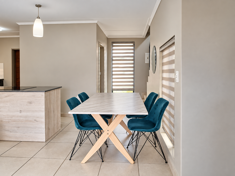 Modern open-plan dining and kitchen area featuring neutral tones, ceramic tile flooring, contemporary pendant lighting, and zebra blinds for adjustable natural light.