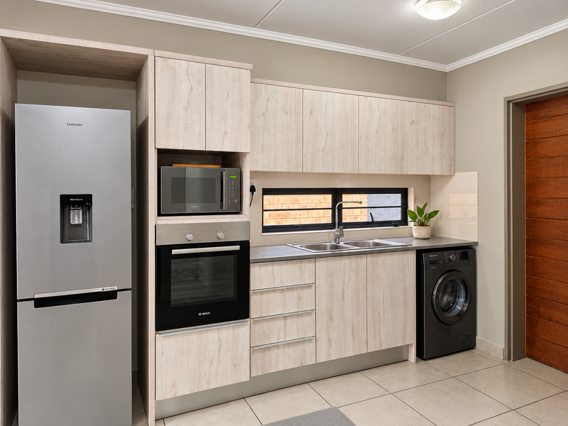 Modern kitchen featuring light wood-grain cabinetry, built-in Bosch oven and microwave, stainless steel sink, and tiled flooring with a clean, contemporary finish.
