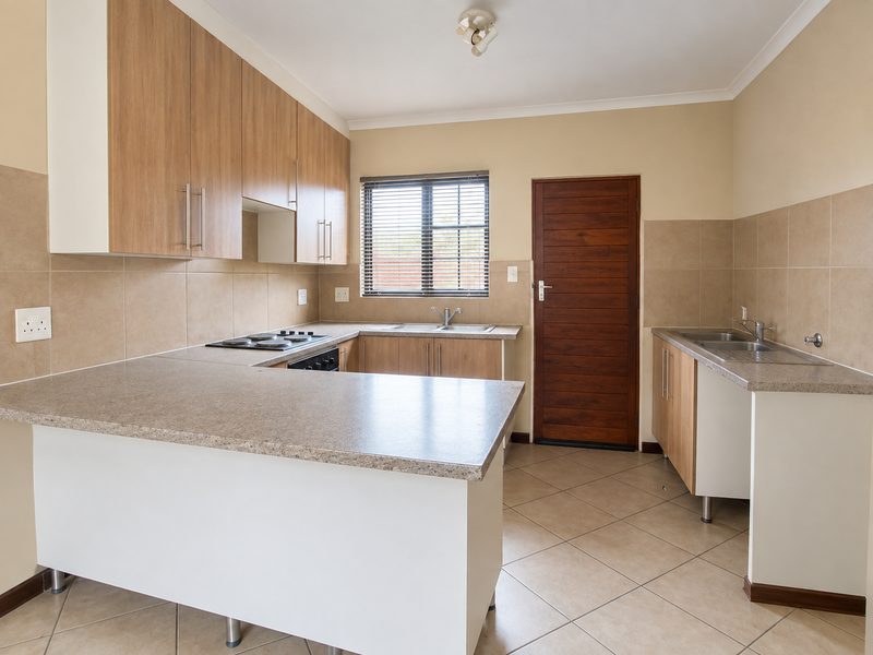 A clean, functional kitchen featuring light wood-look cabinetry, laminate countertops, integrated electric hob and oven, and neutral ceramic floor tiling.