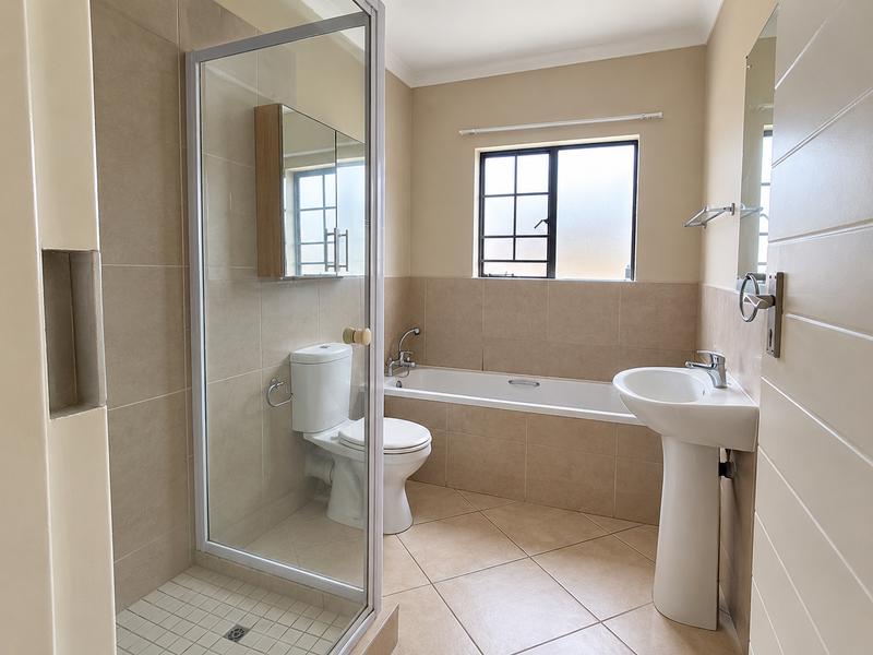 A clean, functional bathroom featuring a pedestal basin, a separate shower enclosure, a bathtub, and neutral wall and floor tiling.