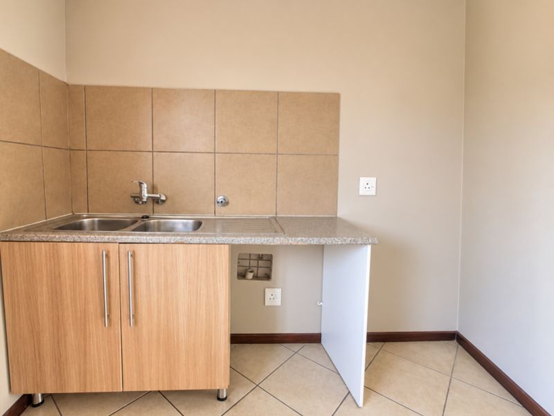 A functional laundry area featuring a stainless steel sink, tiled splashback, and built-in cabinetry with space for an under-counter appliance.