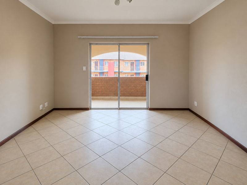 A bright, empty living room featuring neutral tiled flooring, beige walls, and a sliding glass door providing access to an outdoor balcony area.