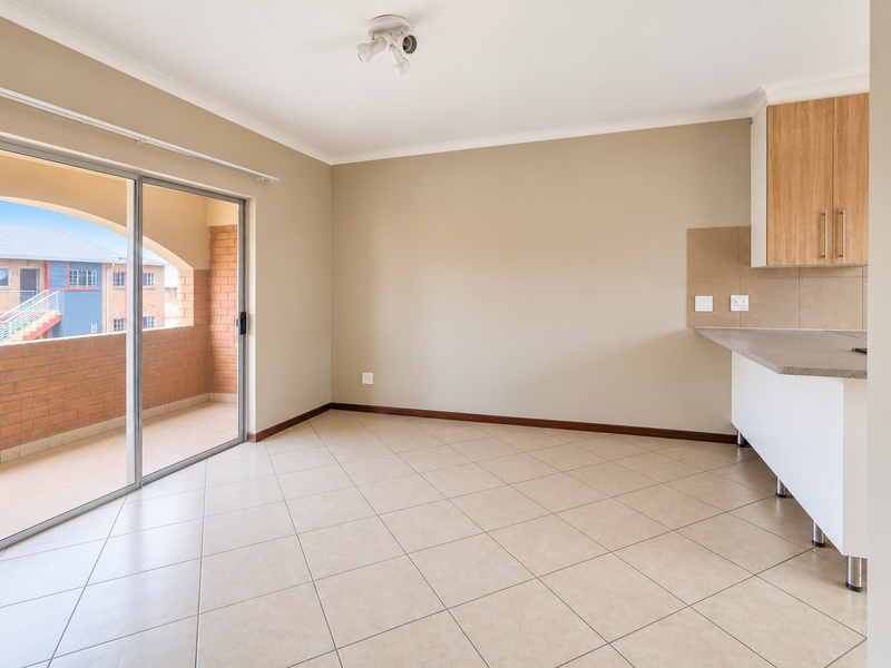 An open-plan living and kitchen area featuring neutral tiled floors, modern cabinetry, and a sliding door leading to a private balcony.