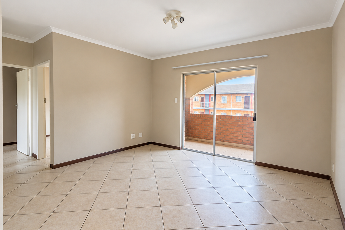 A bright, empty living room featuring neutral tiled flooring, clean walls, and a sliding glass door providing access to an outdoor balcony area.