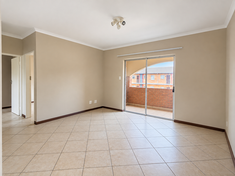 A bright, empty living room featuring neutral tiled flooring, clean walls, and a sliding glass door providing access to an outdoor balcony area.
