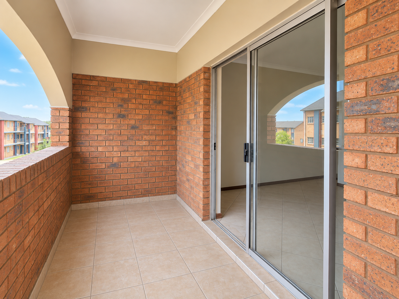 A clean, covered balcony featuring exposed brick walls, tiled flooring, and a large sliding glass door providing access to the interior.