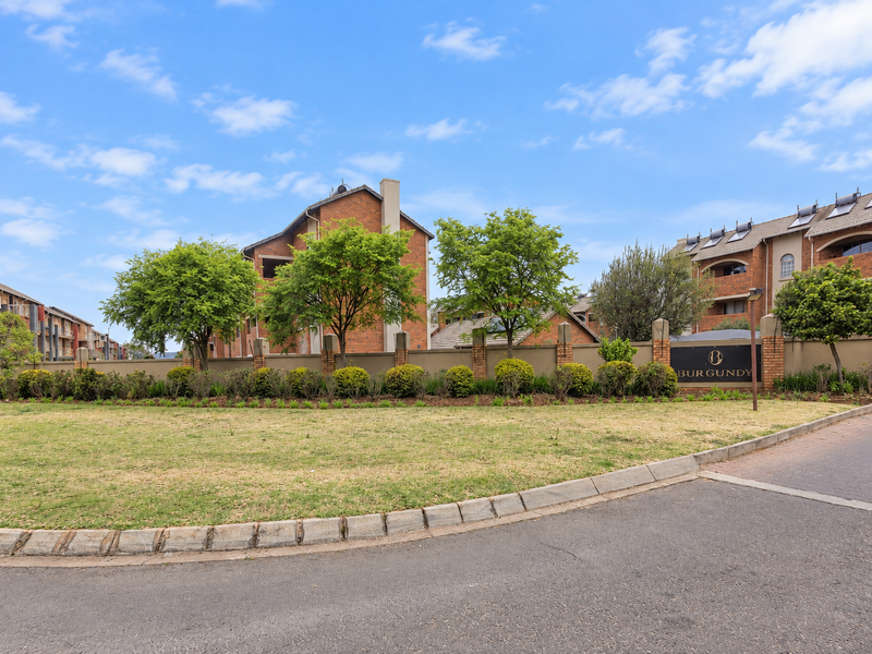 Exterior view of the Burgundy apartment complex featuring brick architecture, landscaped gardens, and a paved entrance area.