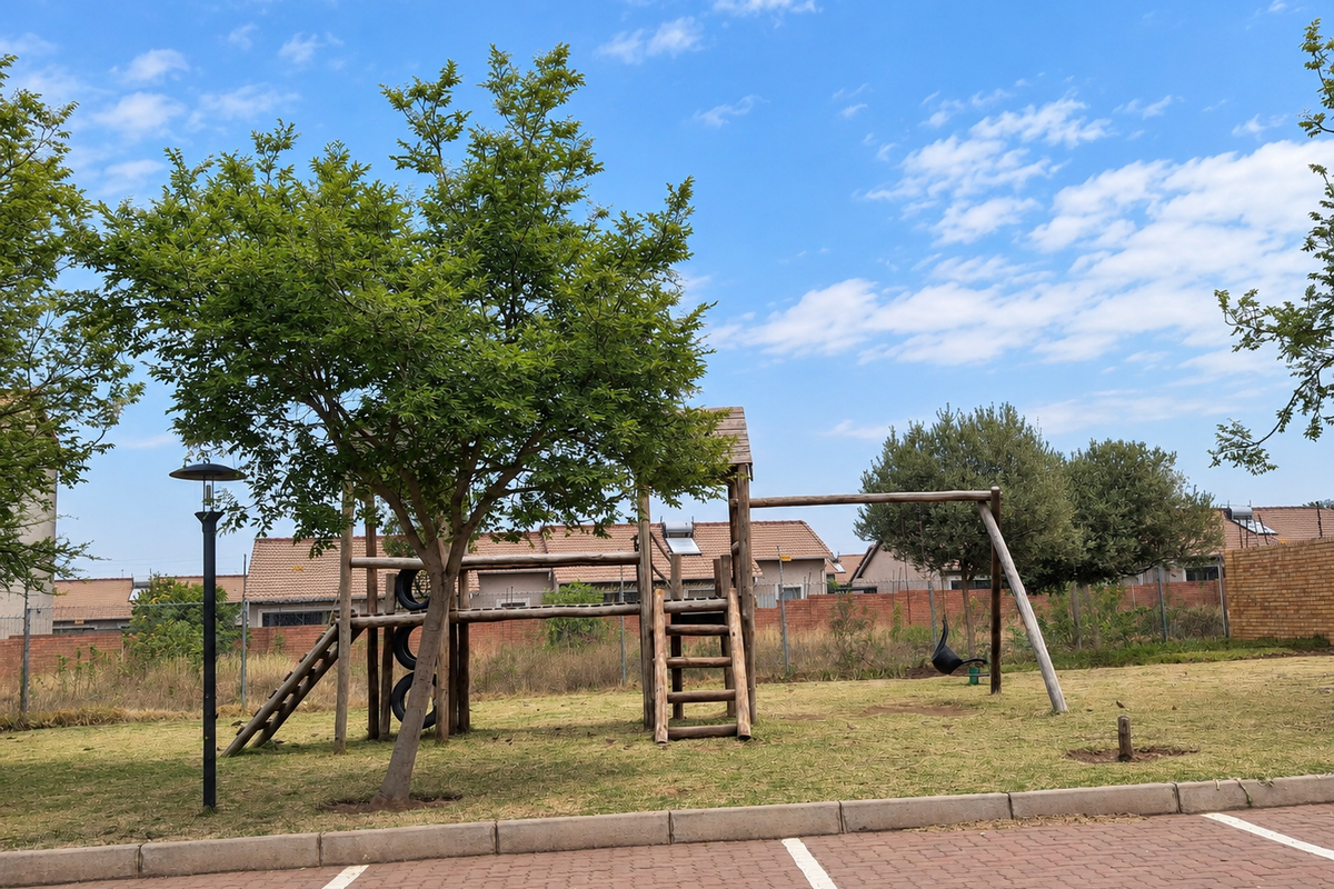 Communal outdoor area featuring a wooden playground structure, paved parking bays, and established garden space with boundary walling.