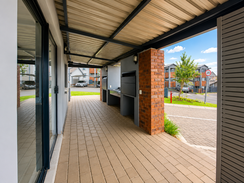 A covered outdoor patio area featuring a built-in braai, paved flooring, and direct access to the exterior through sliding glass doors.