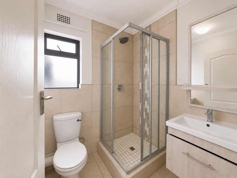A clean and well-maintained bathroom featuring a corner shower enclosure, a modern vanity with a wash basin, and neutral wall and floor tiling.