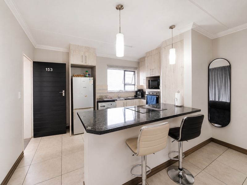 Modern kitchen featuring granite countertops, built-in cabinetry, integrated appliances, and a breakfast bar with pendant lighting, finished with neutral tiled flooring.