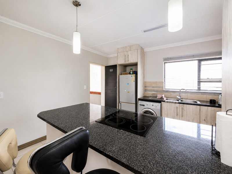 Modern kitchen featuring granite countertops, an integrated electric hob, ample built-in cabinetry, and a stainless steel sink with a tiled backsplash.
