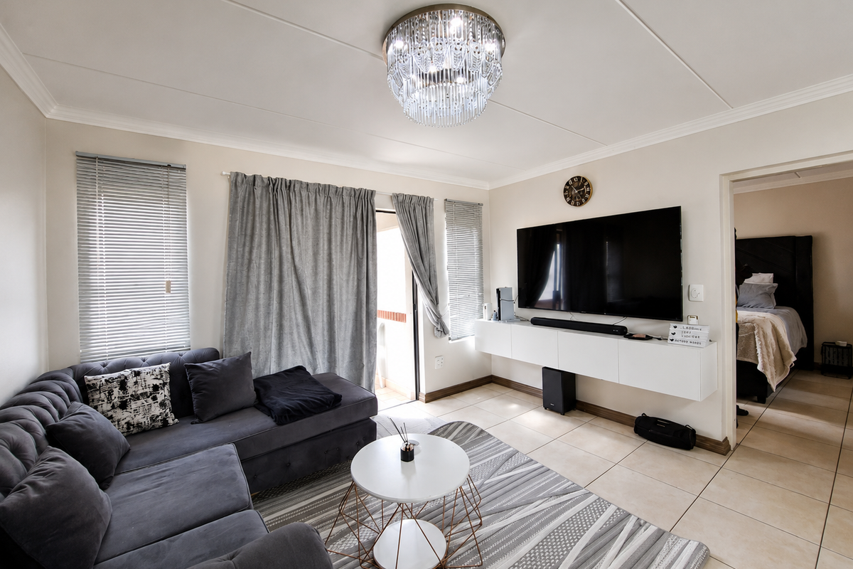 A well-maintained living room featuring tiled flooring, a modern wall-mounted media console, and a decorative crystal chandelier, with direct access to a balcony.