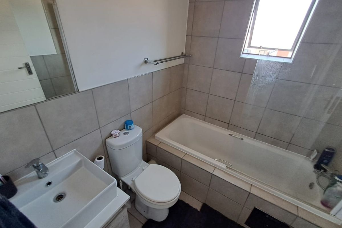 A functional bathroom featuring a built-in bathtub with a glass screen, a wall-mounted basin, and a toilet, finished with neutral wall and floor tiling.