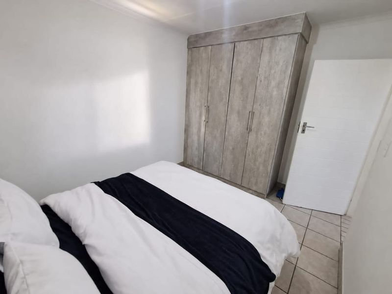 A bedroom featuring built-in cupboards with a wood-look finish and neutral tiled flooring.