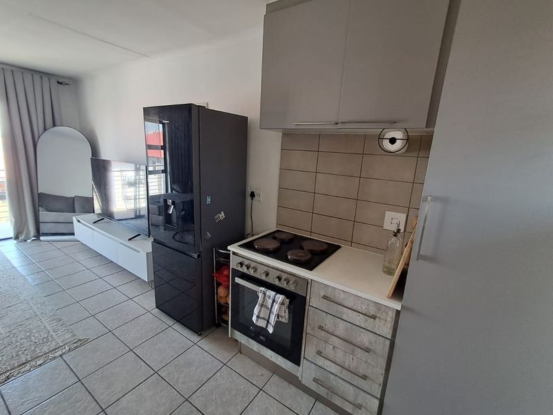 An open-plan living area featuring a compact kitchen with built-in cabinetry, electric hob, oven, and tiled flooring throughout the space.