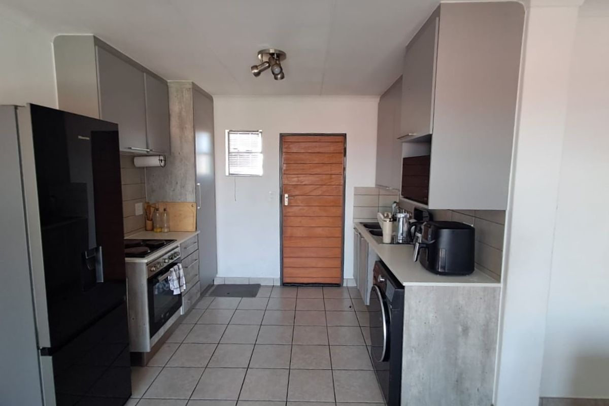 A functional kitchen featuring modern grey cabinetry, tiled flooring, a built-in oven and hob, and dedicated space for laundry appliances.