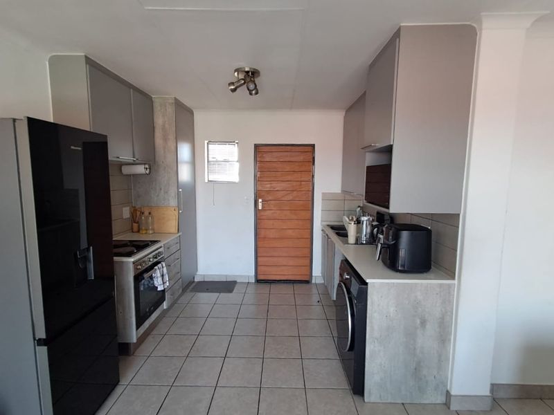 A functional kitchen featuring modern grey cabinetry, tiled flooring, a built-in oven and hob, and dedicated space for laundry appliances.