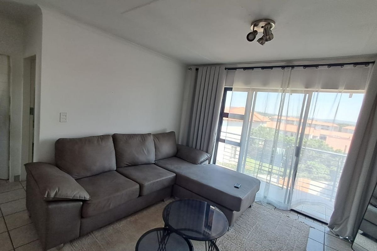 A living room featuring tiled flooring and a large sliding glass door that provides access to a balcony with exterior views.