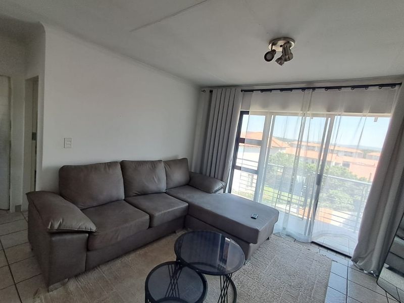 A living room featuring tiled flooring and a large sliding glass door that provides access to a balcony with exterior views.