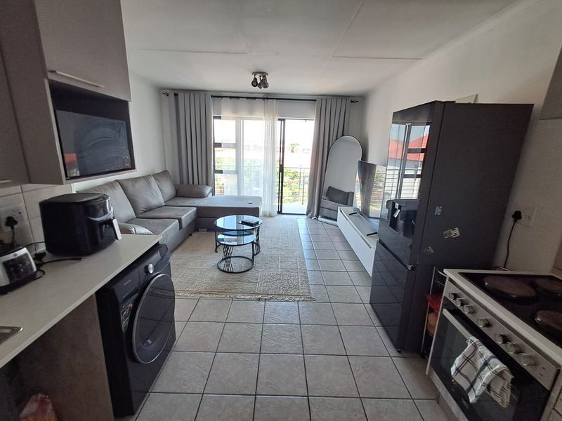 Open-plan living area featuring tiled floors, a functional kitchen layout, and a sliding door leading to a balcony, providing a bright and connected space.