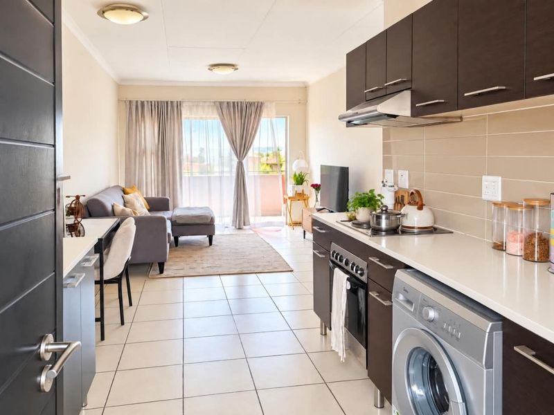Modern open-plan apartment featuring a sleek kitchen with dark cabinetry, integrated appliances, and tiled flooring, flowing seamlessly into a bright living area with balcony access.