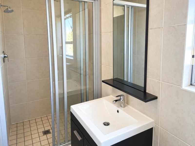 A clean, modern bathroom featuring a glass-enclosed shower, a contemporary vanity with a basin, and neutral wall tiling.